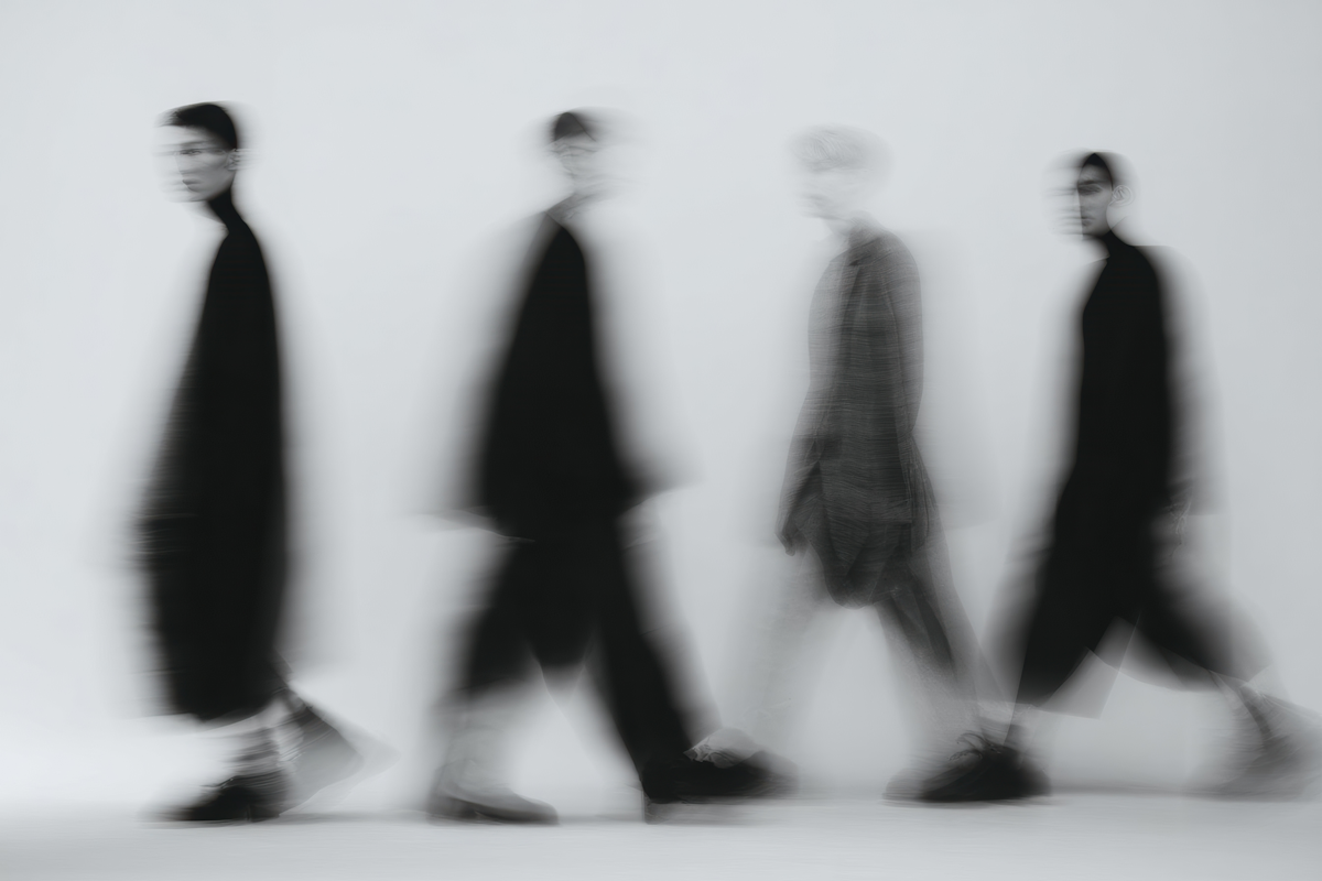 Four blurred figures in suits walking together on a light background