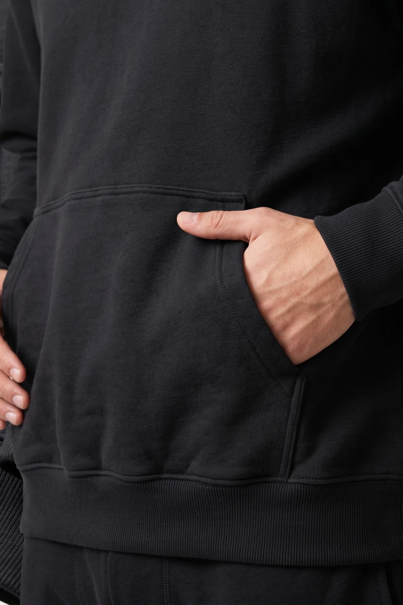 Close-up of a RAQI black pullover hoodie featuring a front kangaroo pocket and ribbed hem detail.
