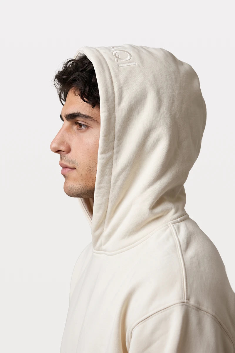Side profile of a man wearing a RAQI creamy beige heavyweight pullover hoodie with tonal branding on the hood
