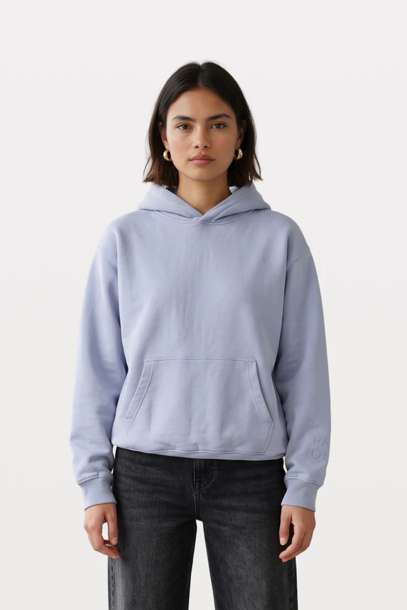 A woman wearing a RAQI sky blue pullover hoodie with a kangaroo pocket and subtle sleeve embroidery.
